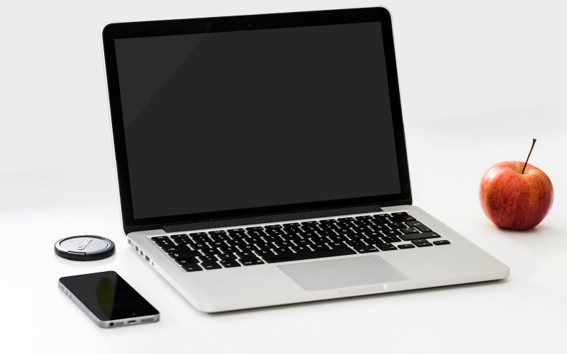 A minimalist workspace featuring a laptop, smartphone, and an apple on a clean white desk.